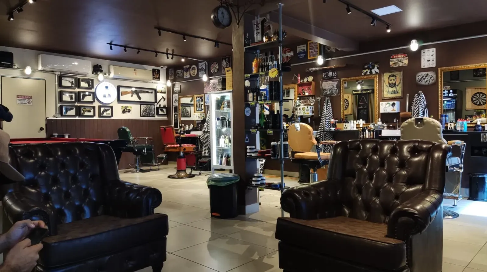 Salão da Barbearia Bernardi à noite, com poltronas Chesterfield de couro e as estações de atendimento ao fundo